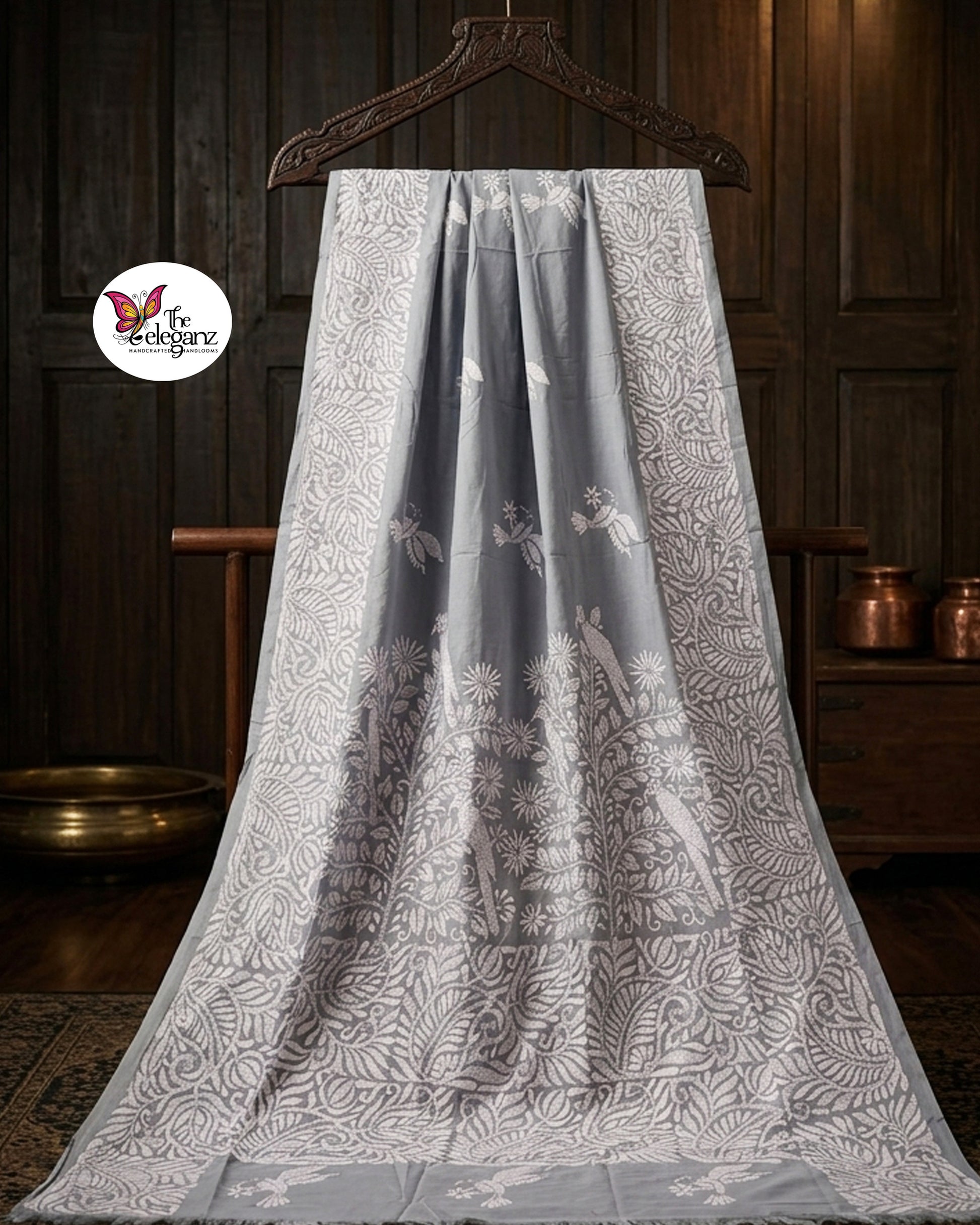 Woman draped in a steel grey blended Bangalore silk saree featuring intricate white Kantha embroidery with bird, floral, and foliage motifs across the border and pallu.