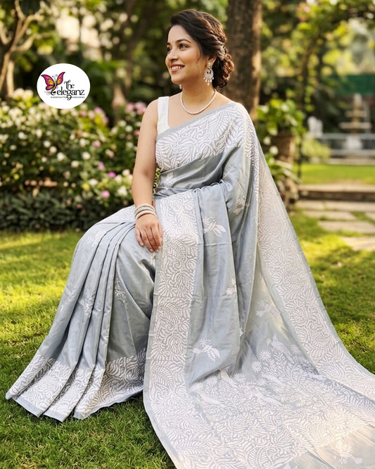 Woman draped in a steel grey blended Bangalore silk saree featuring intricate white Kantha embroidery with bird, floral, and foliage motifs across the border and pallu.