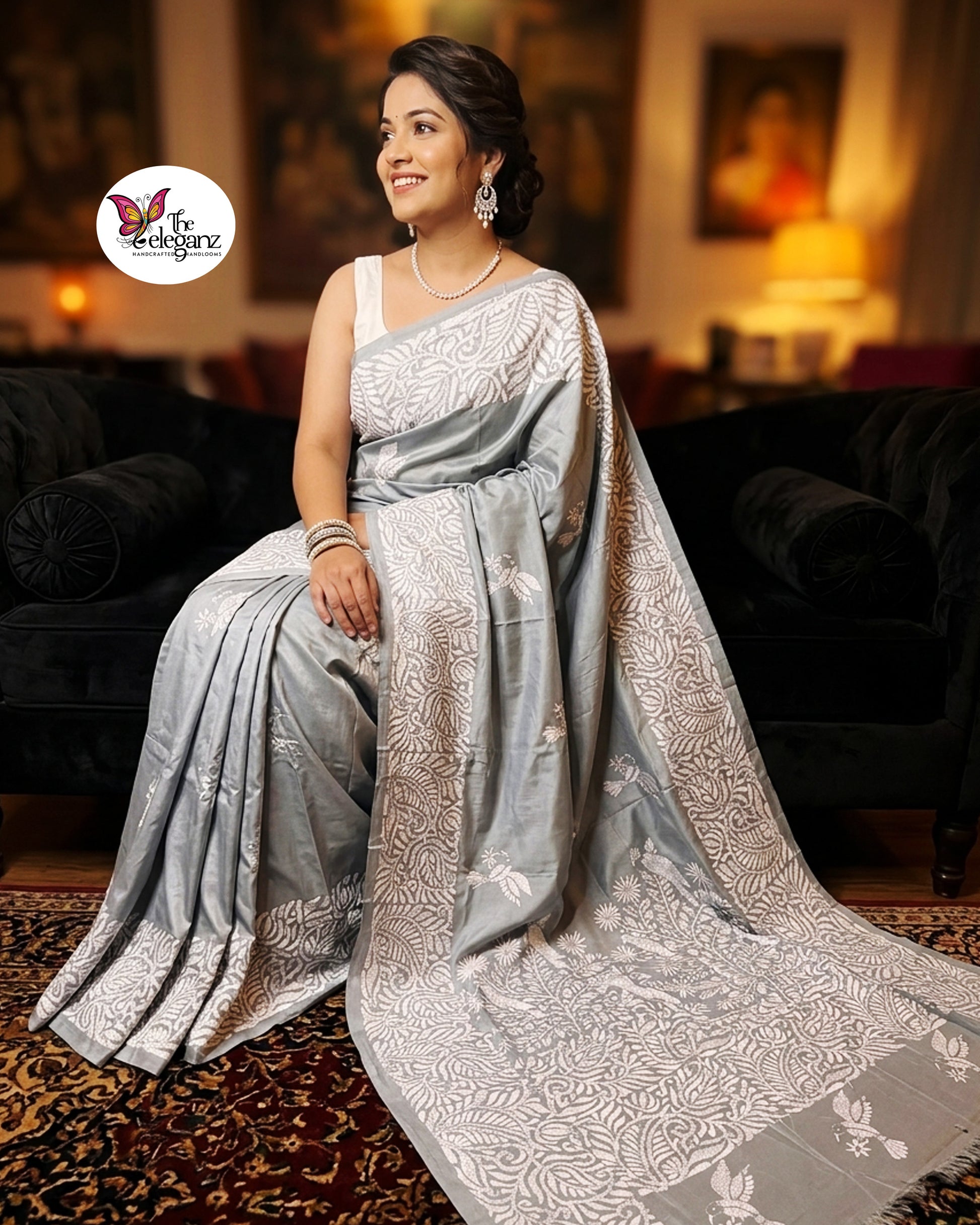 Woman draped in a steel grey blended Bangalore silk saree featuring intricate white Kantha embroidery with bird, floral, and foliage motifs across the border and pallu.