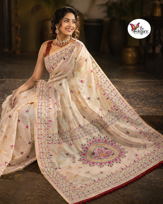 Woman draped in an ivory white embroidered semi silk saree featuring multicolour floral motifs, geometric borders, and an ornate embroidered pallu design.