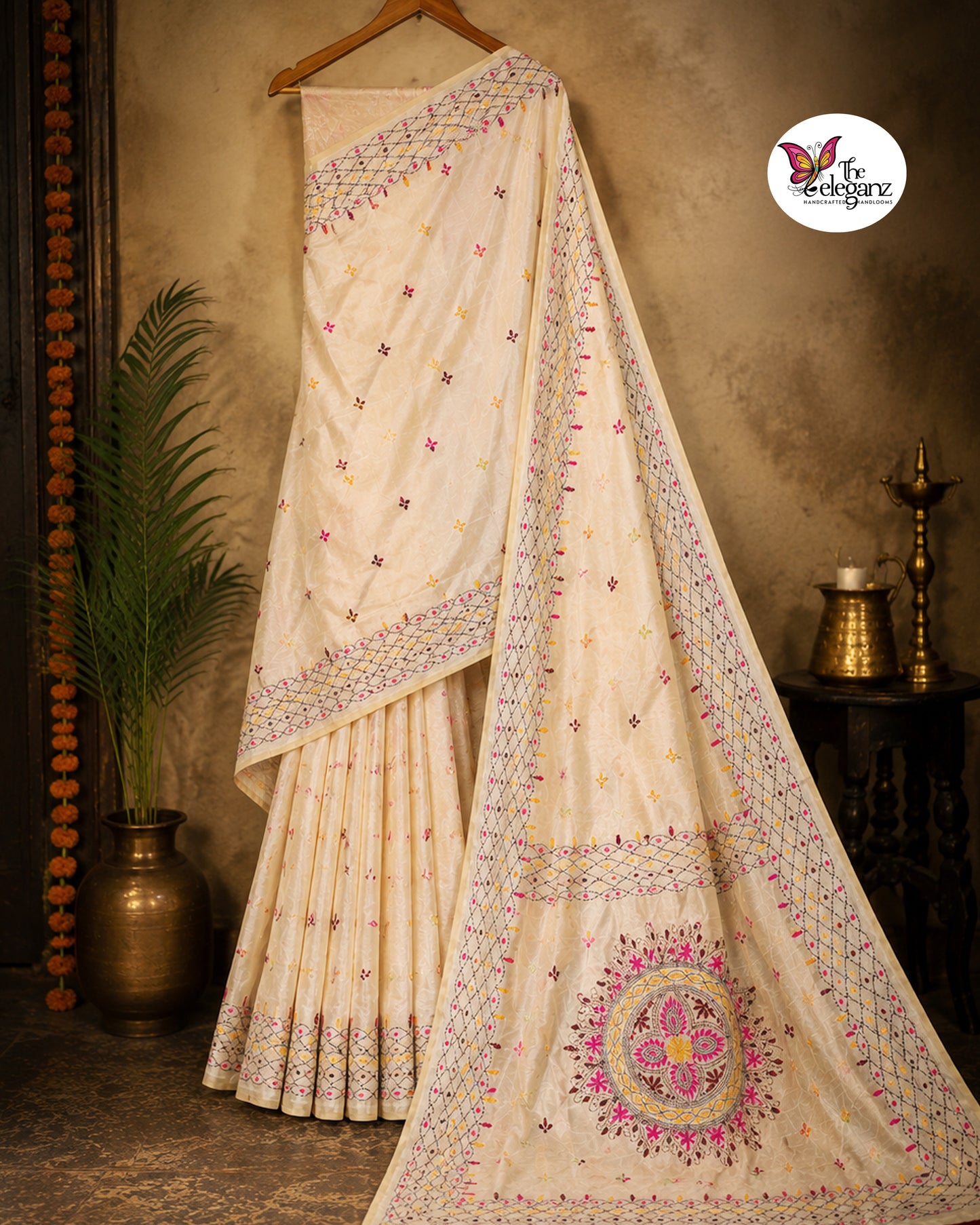 Woman draped in an ivory white embroidered semi silk saree featuring multicolour floral motifs, geometric borders, and an ornate embroidered pallu design.