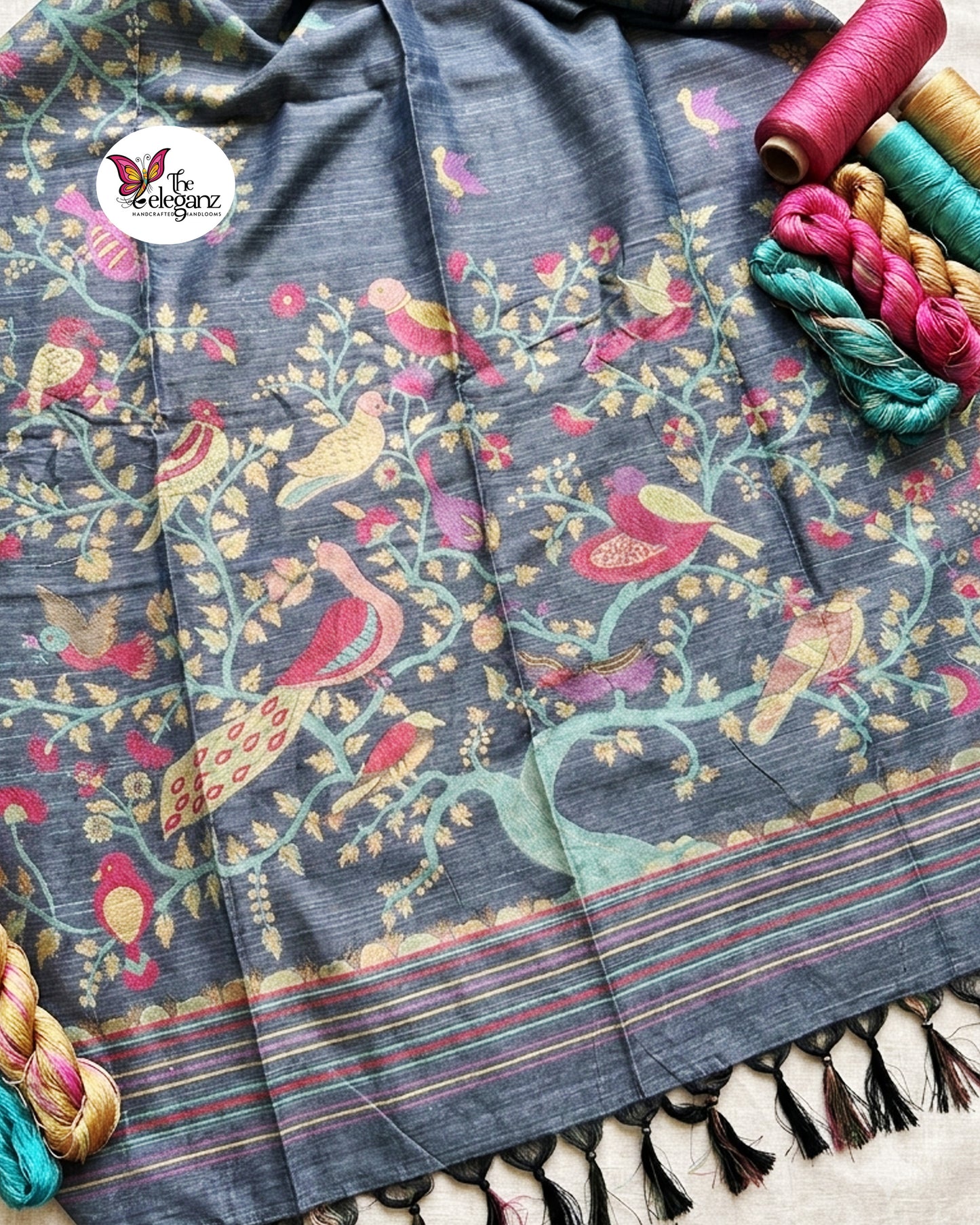 Woman draped in a smoky grey semi tussar silk saree featuring woven bird, floral, and vine motifs across the border and pallu with matching blouse piece.