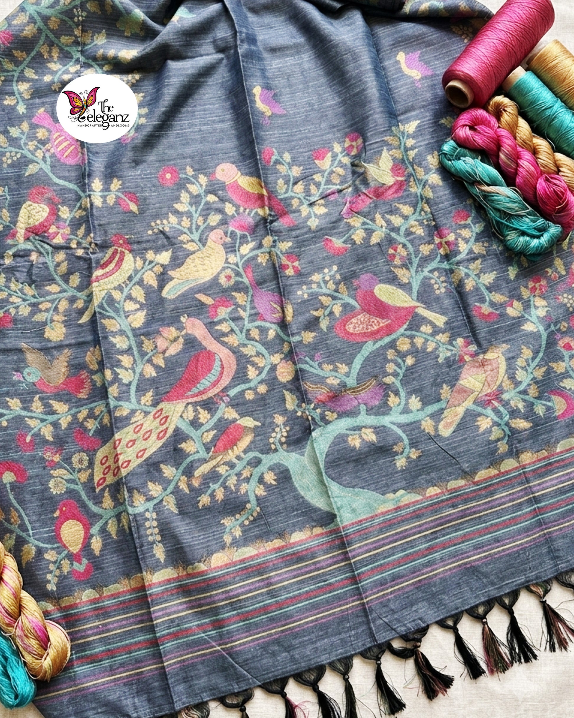 Woman draped in a smoky grey semi tussar silk saree featuring woven bird, floral, and vine motifs across the border and pallu with matching blouse piece.