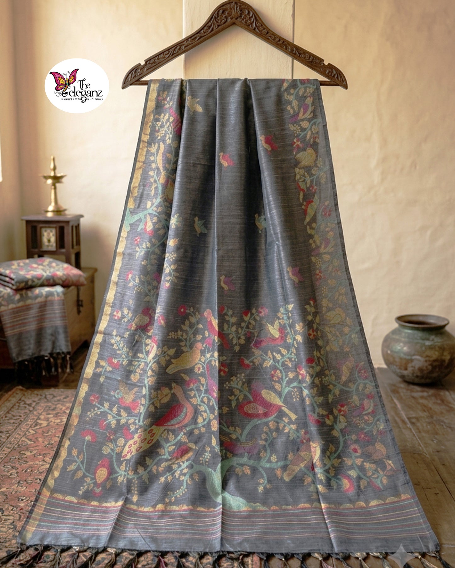 Woman draped in a smoky grey semi tussar silk saree featuring woven bird, floral, and vine motifs across the border and pallu with matching blouse piece.