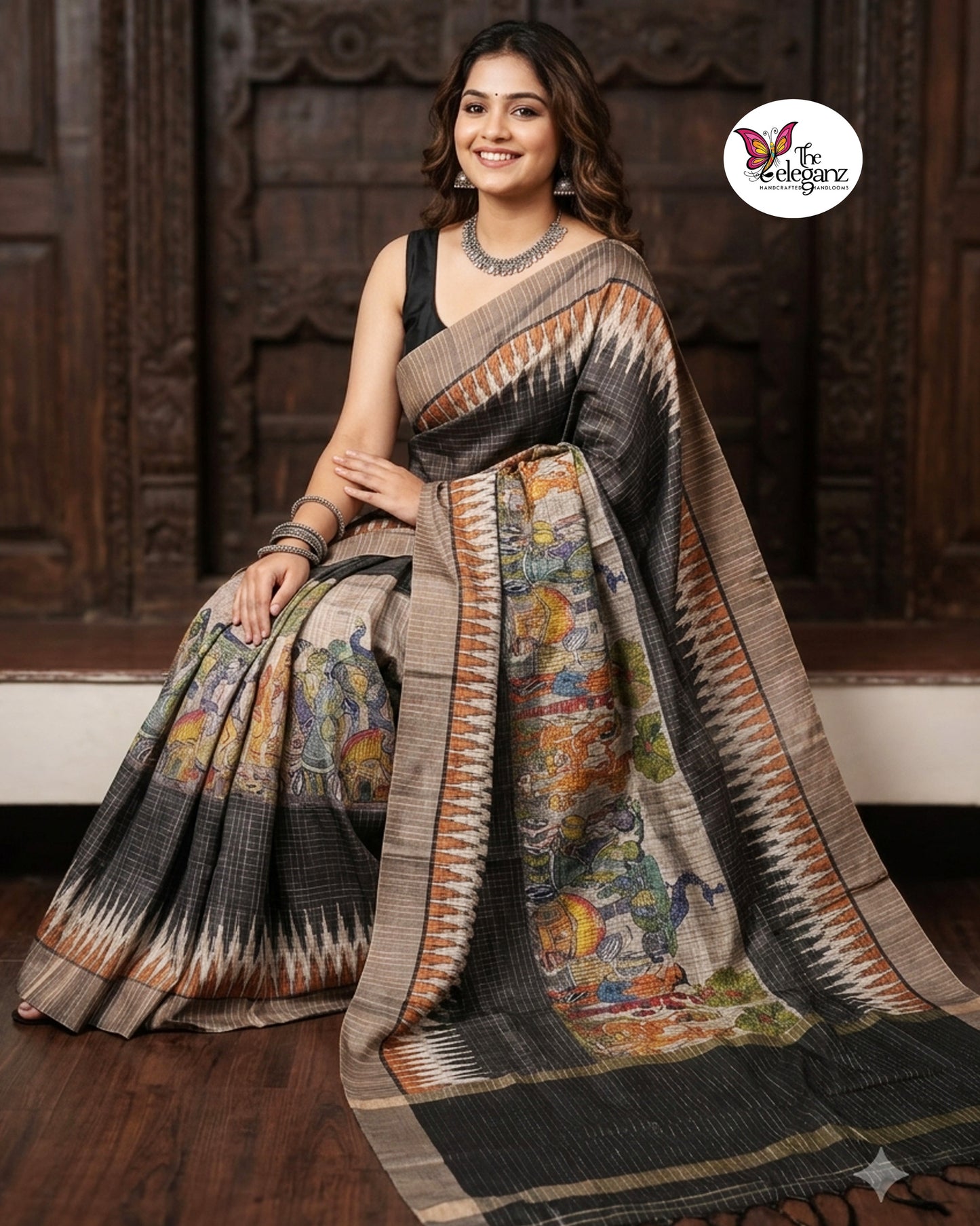 Woman draped in a charcoal-grey checked semi tussar silk saree featuring heritage-inspired print work with peacock motifs, folk art panels, and matching blouse piece.
