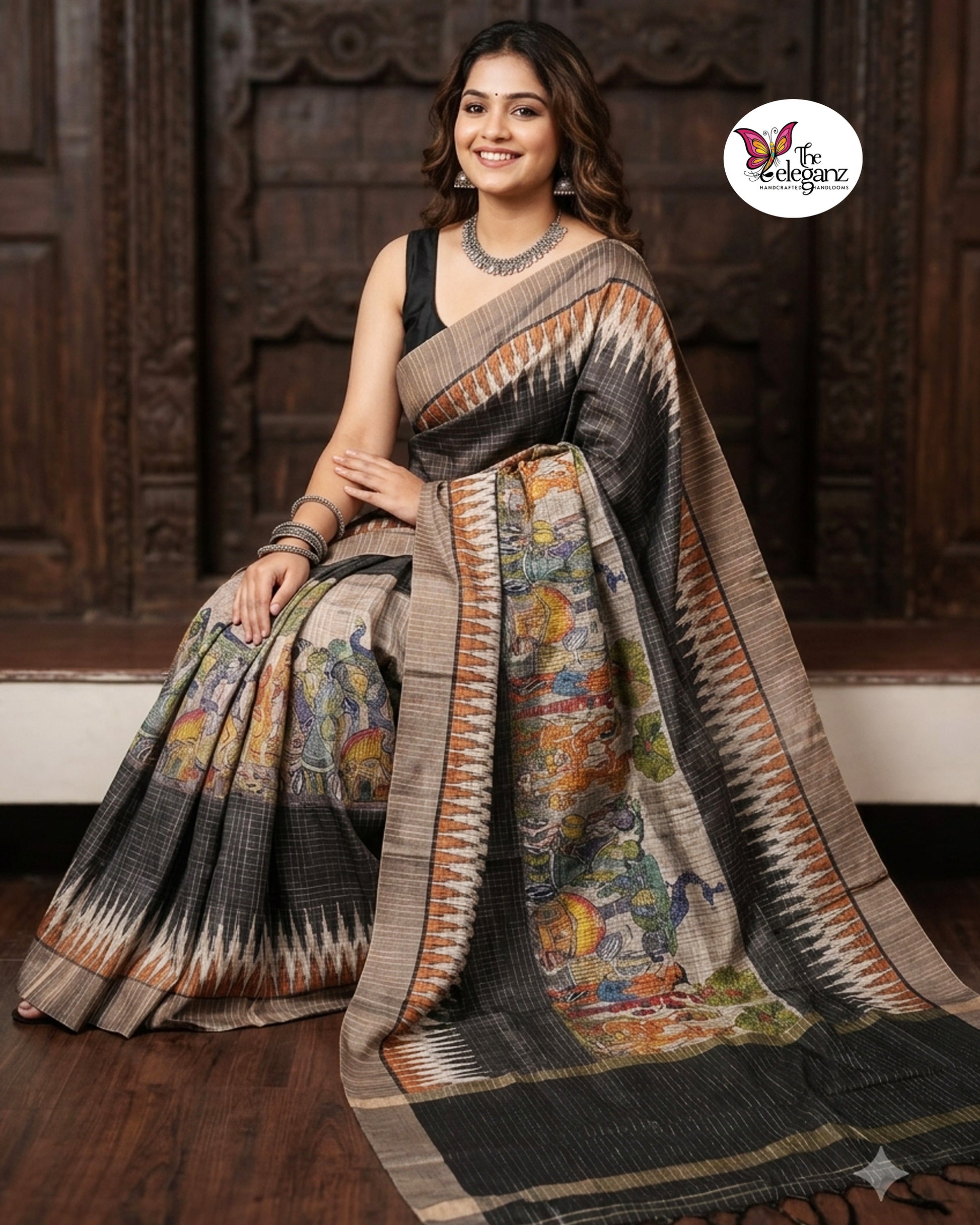 Woman draped in a charcoal-grey checked semi tussar silk saree featuring heritage-inspired print work with peacock motifs, folk art panels, and matching blouse piece.