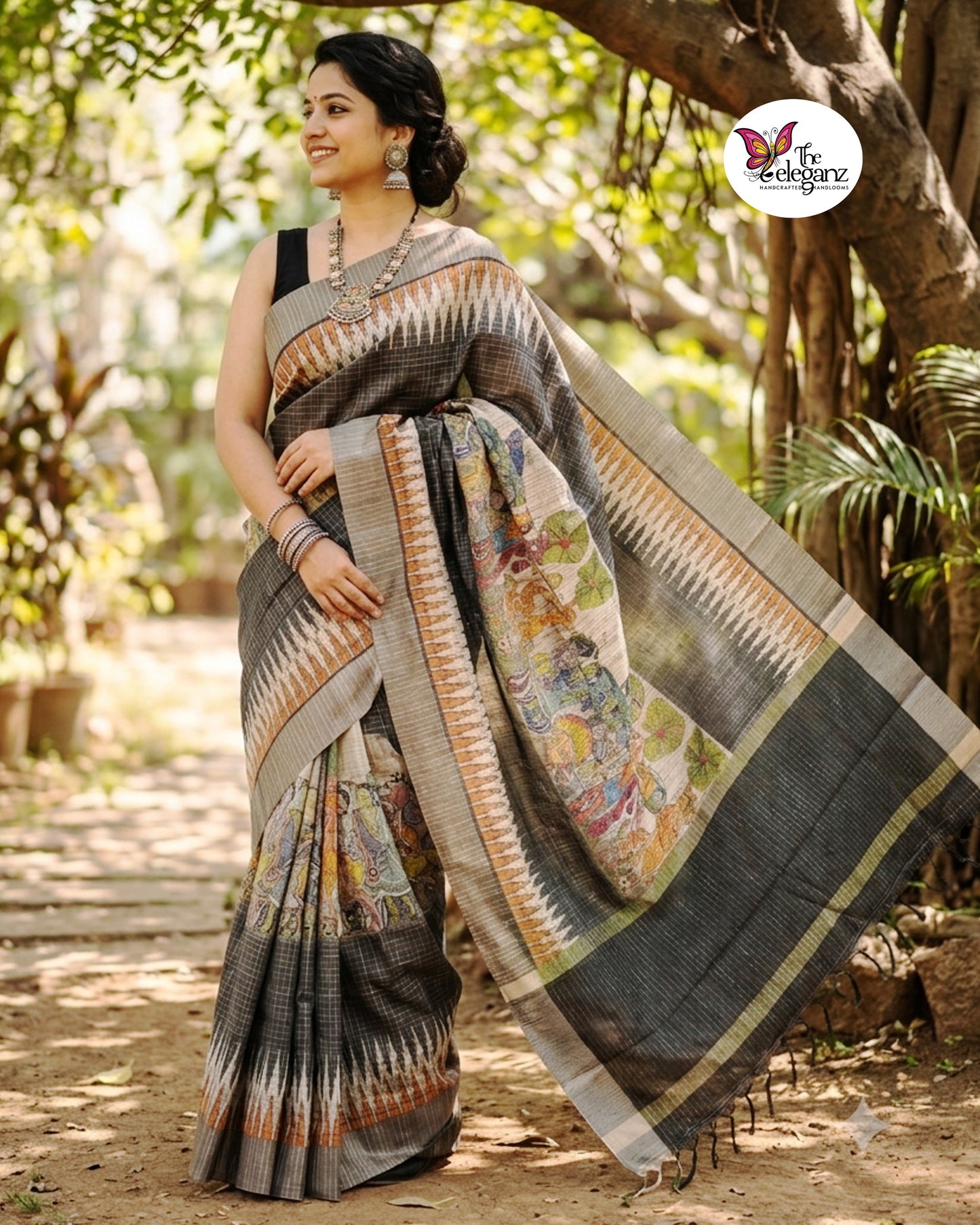 Woman draped in a charcoal-grey checked semi tussar silk saree featuring heritage-inspired print work with peacock motifs, folk art panels, and matching blouse piece.