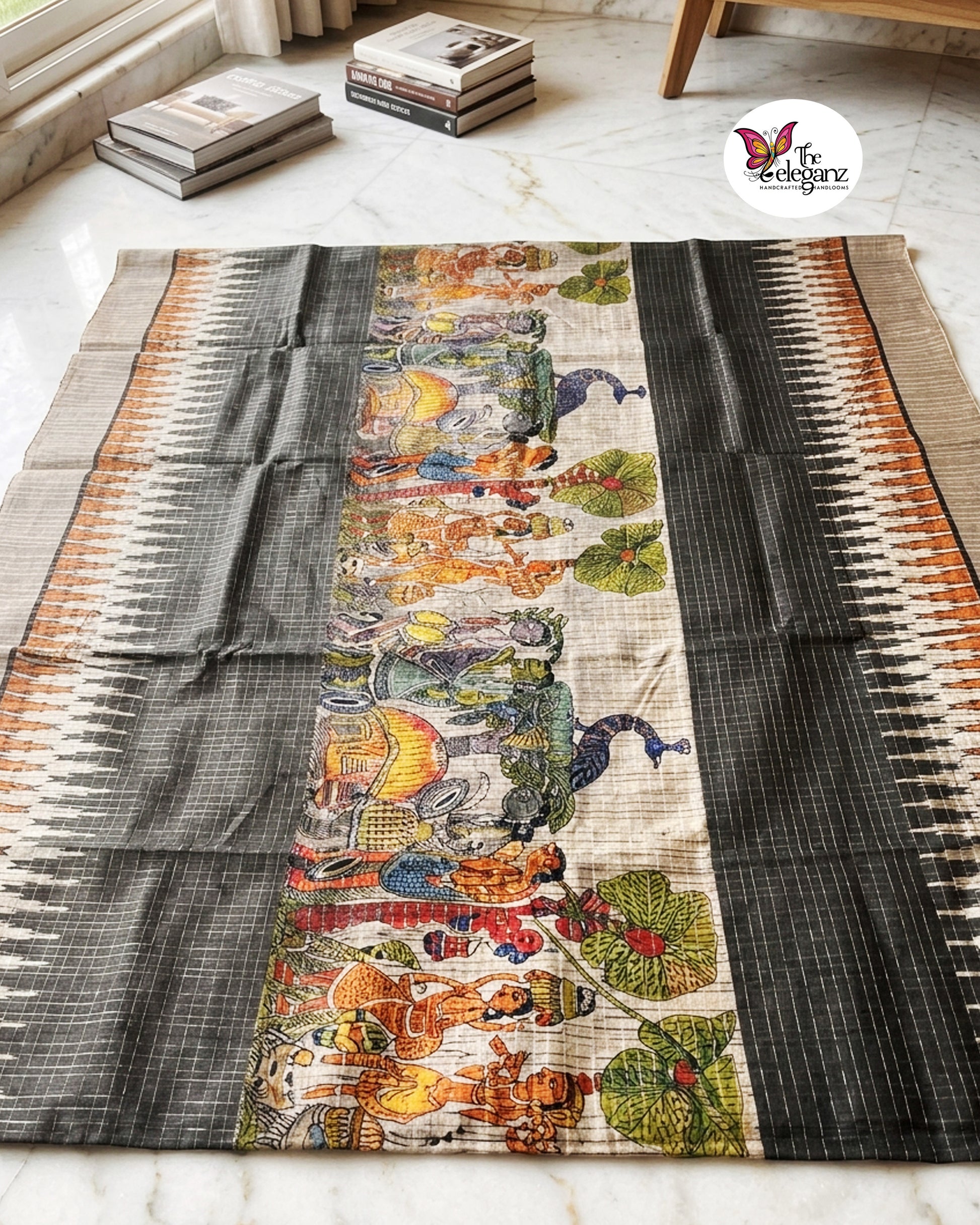 Woman draped in a charcoal-grey checked semi tussar silk saree featuring heritage-inspired print work with peacock motifs, folk art panels, and matching blouse piece.
