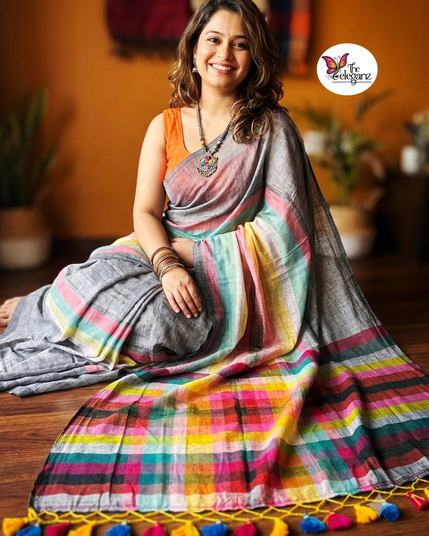 Woman draped in an ash-grey Mul Cotton saree featuring vibrant multicolour striped pallu and border with handcrafted colourful tassels.