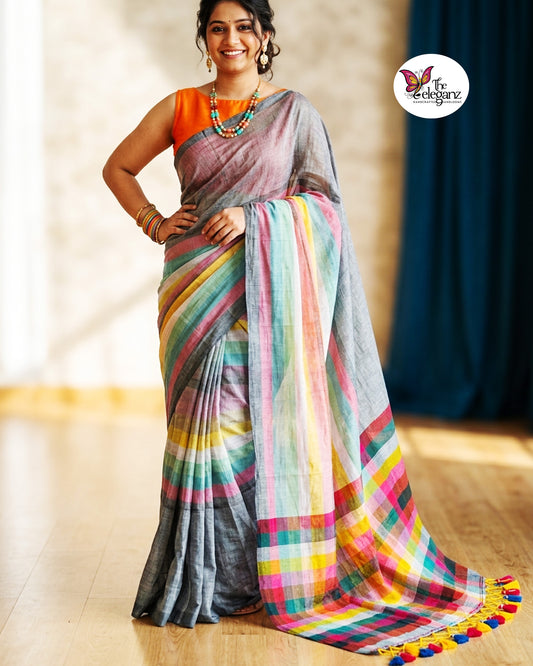 Woman draped in an ash-grey Mul Cotton saree featuring vibrant multicolour striped pallu and border with handcrafted colourful tassels.