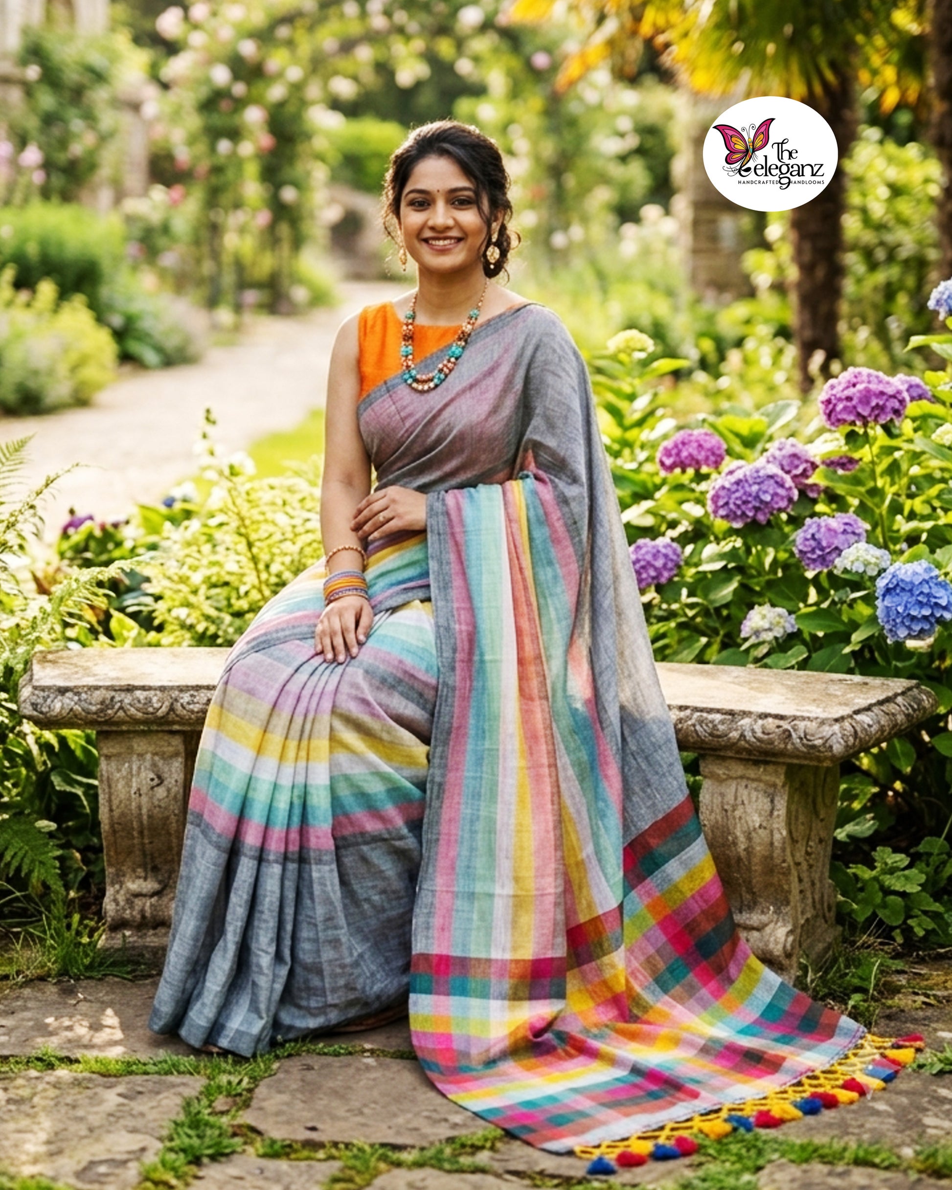 Woman draped in an ash-grey Mul Cotton saree featuring vibrant multicolour striped pallu and border with handcrafted colourful tassels.